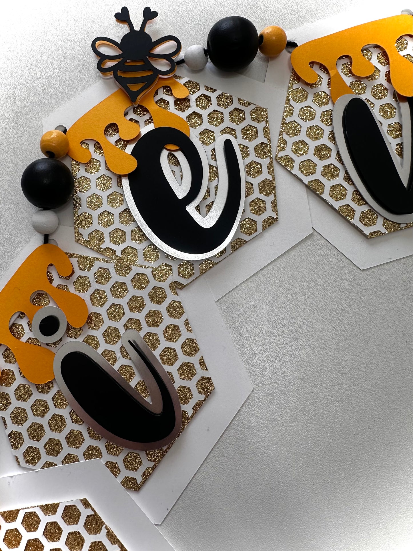 Bee-lieve handmade honeybee paper banner with glitter accents in black, yellow, and gold
Close-up of layered cardstock honeycomb details on Bee-lieve banner
Bee-lieve banner displayed as party décor with ribbon tassels and bead accents
Honeybee banner hanging in a nursery or classroom setting
Bee-lieve banner styled on a tiered tray for home décor
Full view of Bee-lieve honeybee garland banner for bee-themed celebrations